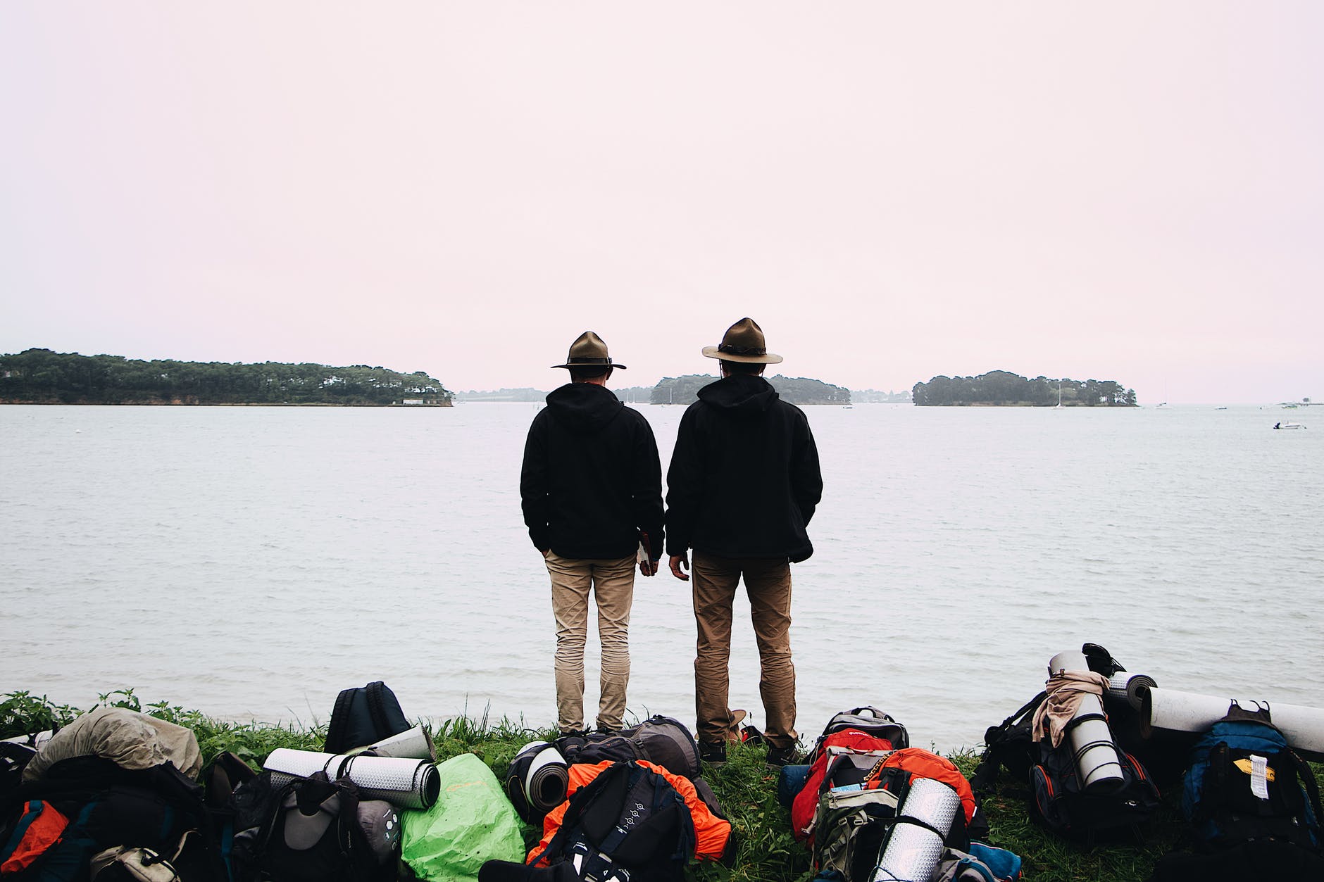 two men with hats and black jackets stand near body of water